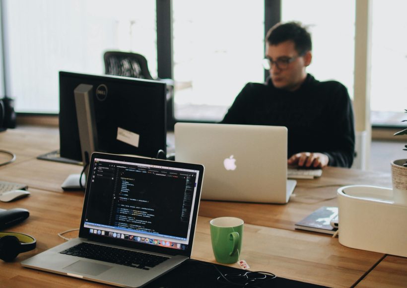 man in black shirt sits behind desk with computers